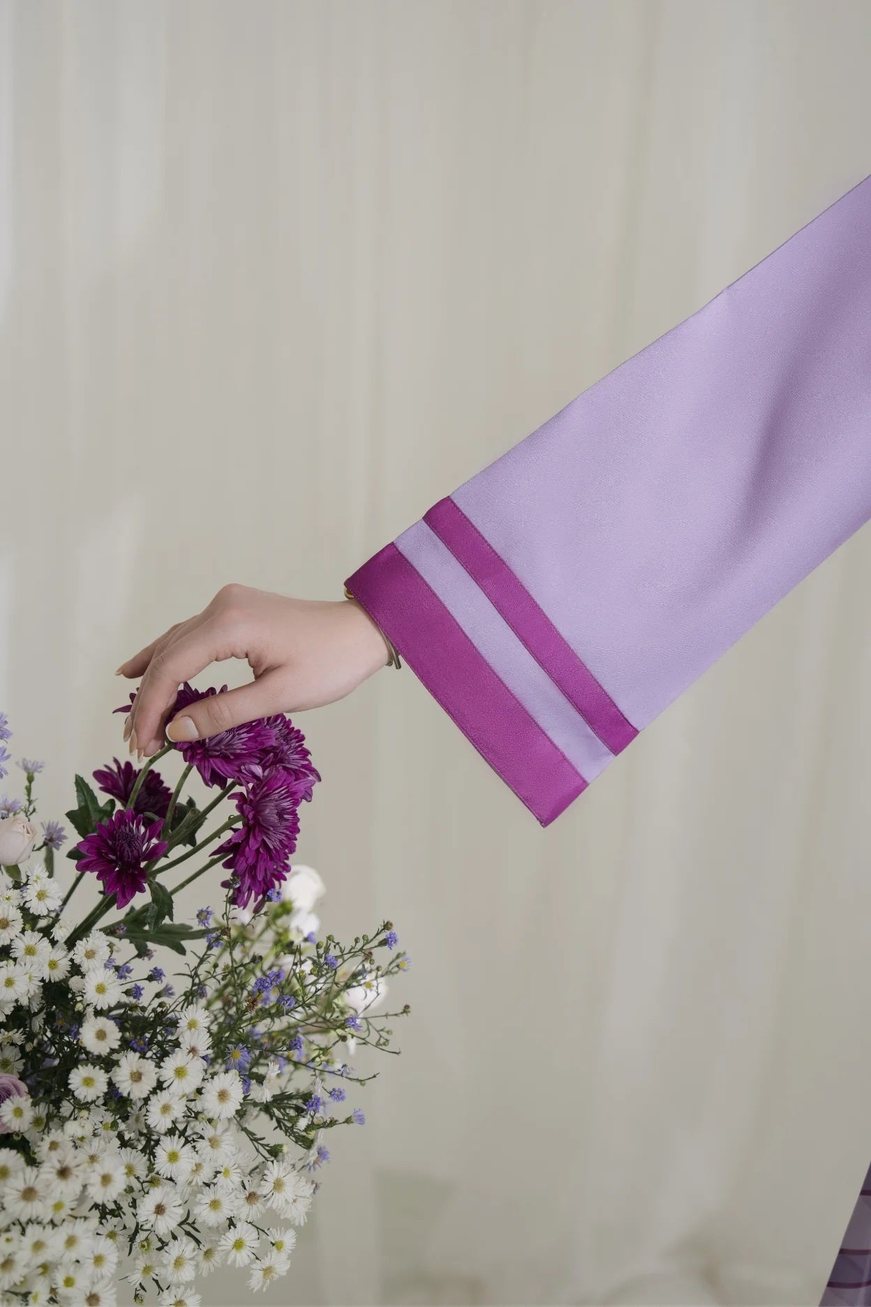 Person wearing a purple garment holding a bouquet of flowers against a plain background
