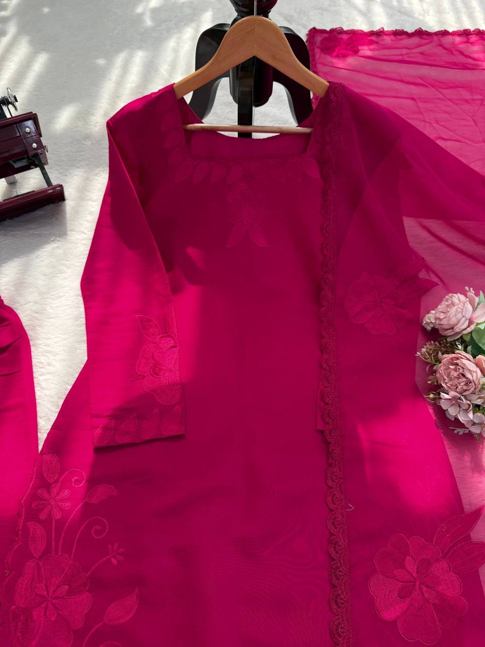 Pink embroidered fabric on a hanger with flowers in the background