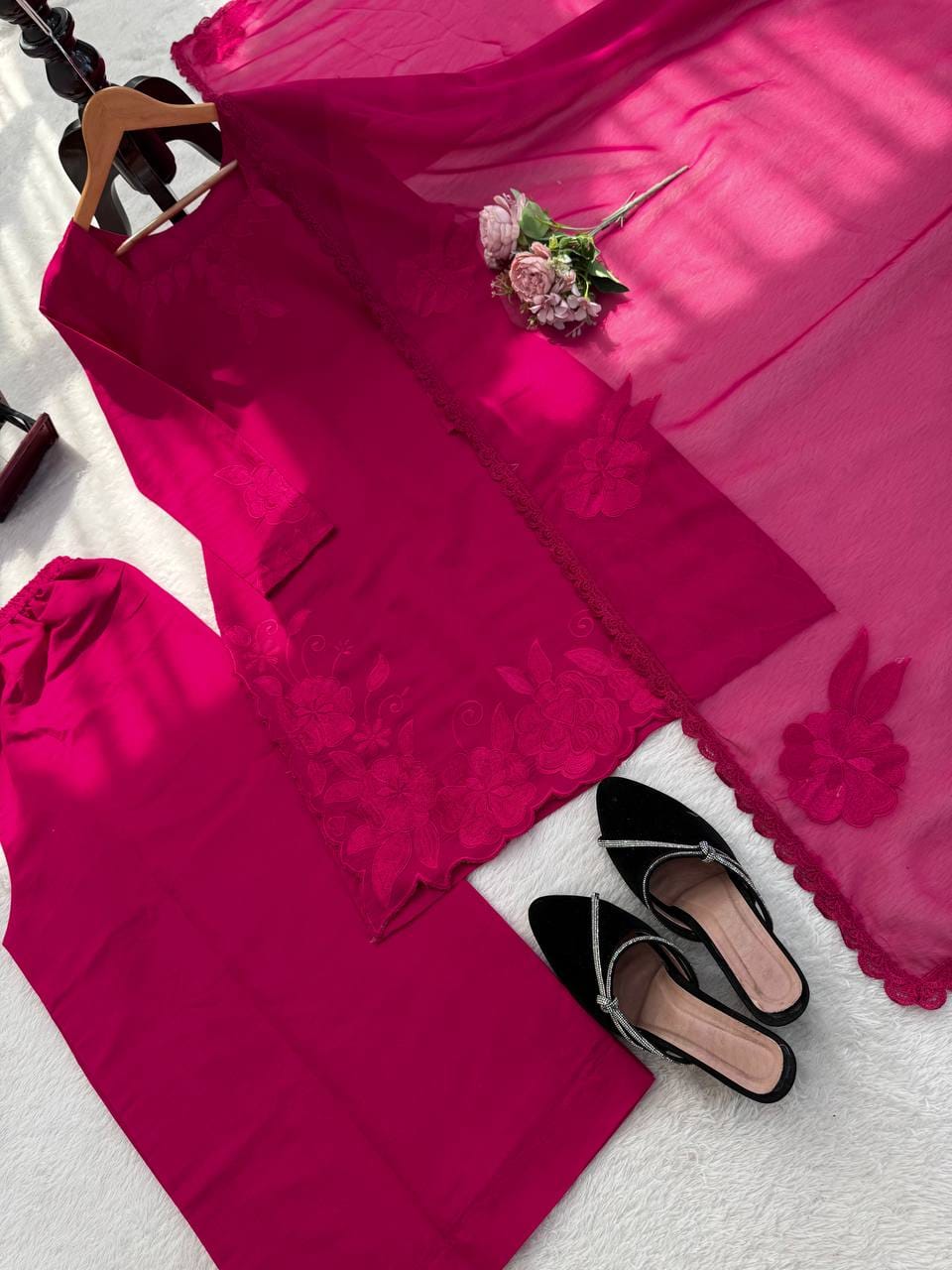Fuchsia dress with floral details on a white surface, accompanied by black shoes and a bouquet.