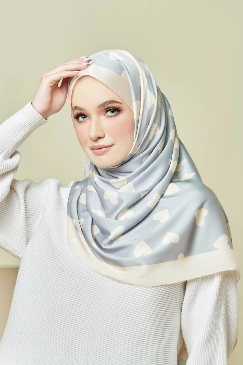 Woman wearing a light gray hijab with white polka dots on a beige background