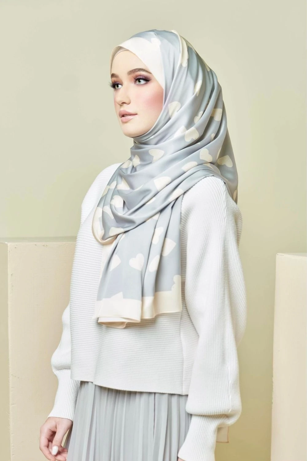 Woman wearing a light gray hijab with white polka dots on a plain background