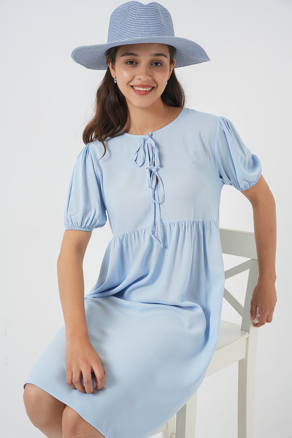 Woman wearing a light blue dress and hat against a white background
