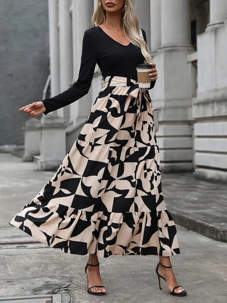 Woman wearing a black long-sleeve top and a long, patterned skirt with a blurred building background