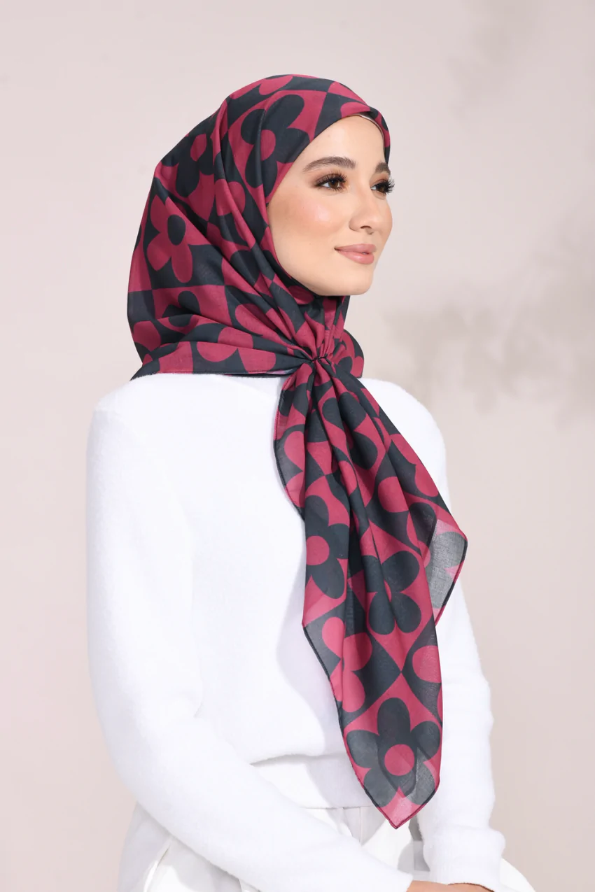 Woman wearing a red and black patterned hijab on a plain background