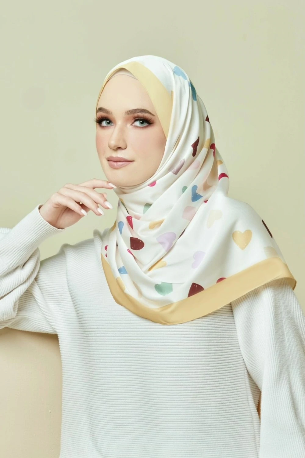 Woman wearing a patterned hijab with heart designs on a plain background