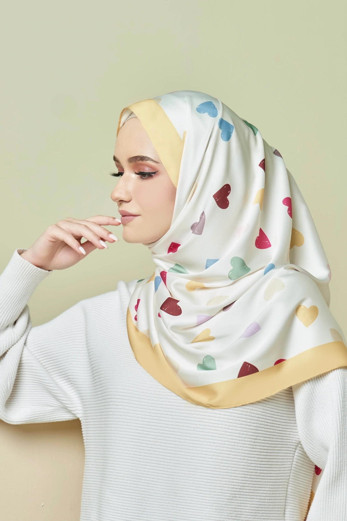 Woman wearing a white hijab with colorful heart patterns on a light green background
