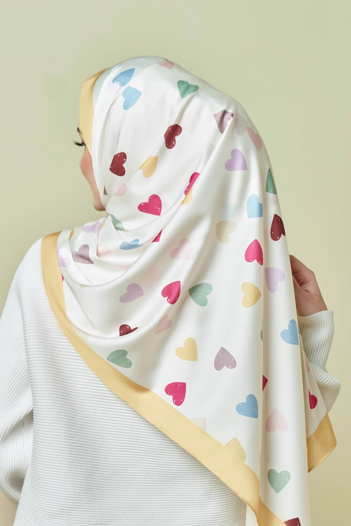 Person wearing a headscarf with colorful heart patterns on a plain background
