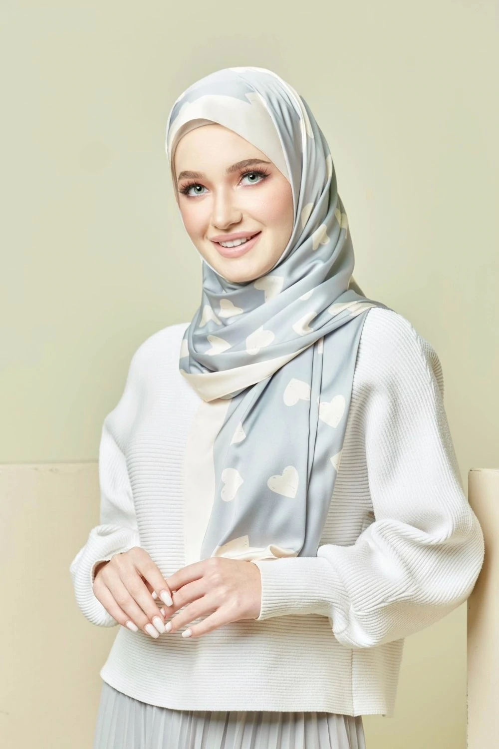 Woman wearing a light gray hijab with heart patterns on a beige background